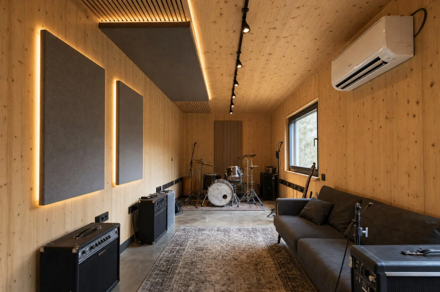 ONE Live interior: visible spruce walls, grey acoustic panels with backlight, a drum kit, amps and a sofa